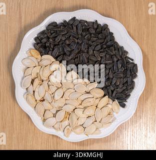 Close-up of edible seeds on a round plate where black sunflower seeds meet white pumpkin seeds in a perfect division, symbolizing balance and healthy Stock Photo