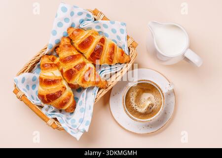 Aromatic croissants in wicker basket with cup of coffee on light background, cozy breakfast scene Stock Photo