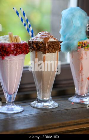 Three different flavored milkshakes with whipped cream and sprinkles on top. The pink one is the lightest and the blue one is the darkest Stock Photo