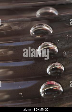 Macro shot of clear water droplets resting on a dark, ribbed metallic surface. Abstract textures and reflections creating a modern industrial look. Stock Photo