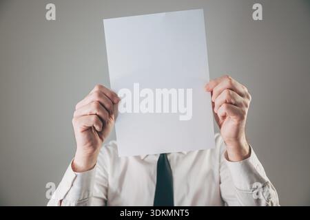 Businessman hiding face behind blank white paper sheet mockup, selective focus Stock Photo