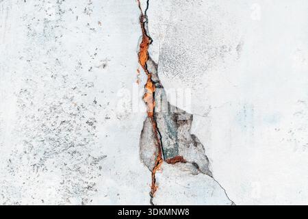 Texture of a weathered gray concrete wall split by a deep jagged crack as background Stock Photo