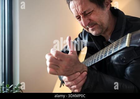 Musician in pain clutching wrist while holding acoustic guitar, selective focus Stock Photo