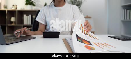 Business Analysis. Young woman reviewing financial documents and using a calculator. Stock Photo