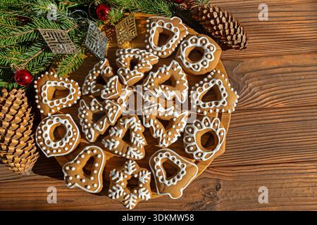 Iced Christmas Cookies with Rustic Decorations. Decorative gingerbread cookies with white icing shaped as bells, trees, and hearts, placed on a wooden Stock Photo