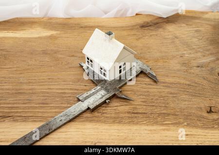 Metal caliper measuring a white model house on a wooden desk, construction cost  concept Stock Photo