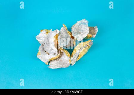 Aluminium tin foil, many empty chocolate candy packaging pile on blue background Stock Photo