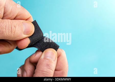 Velcro fastener tape with hook and loop tape openeb by male fingers on blue background, soft focus Stock Photo