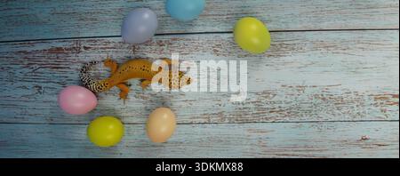 Leopard gecko positioned on a wooden surface with pastel-colored Easter eggs scattered around Stock Photo