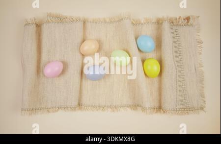 Colorful plastic eggs in pastel shades placed on a textured beige fabric with fringed edges, suitable for Easter and spring-themed decorations Stock Photo