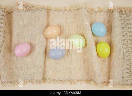 Easter holiday background. Pastel-colored eggs are placed on a woven fabric table runner Stock Photo