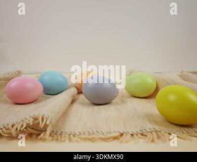 Easter holiday background. Pastel colored eggs are placed on a burlap cloth with a neutral background Stock Photo