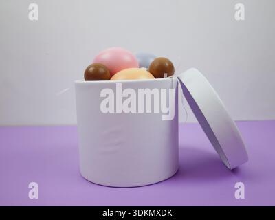 Easter holiday background. White round box with colorful eggs inside on a purple surface Stock Photo