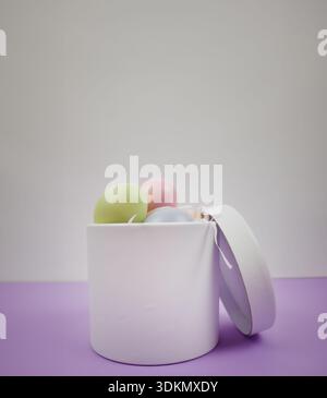 Easter holiday background. White gift box contains pastel colored eggs on a purple surface Stock Photo