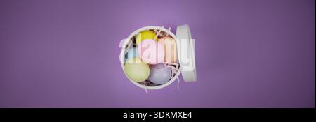 Easter holiday background. Colorful eggs are arranged in a white basket on a purple background Stock Photo