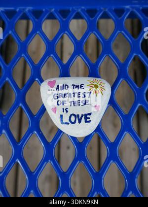 And the greatest of these is love kindness rock over blue metal mesh background vertical photo Stock Photo