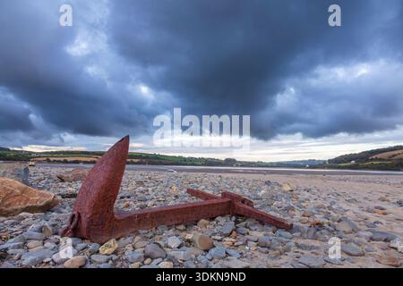 Old rusty anchor sits under dark clouds at the mouth of the river Teifi. The Patch, Gwbert on Sea, Ceredigion. Stock Photo