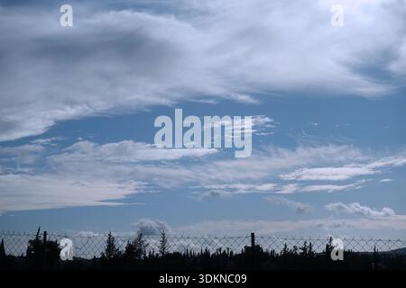 Fence and tree silhouettes under cloudy blue sky. Stock Photo