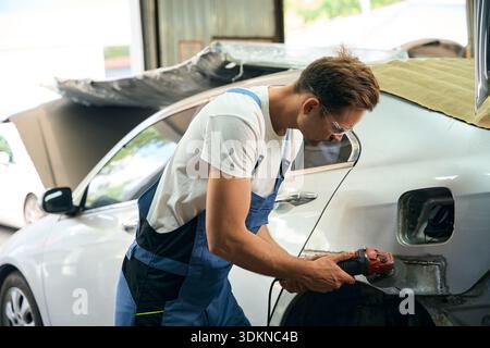 Mechanic working with angle grinder to fix metal body in garage Stock Photo