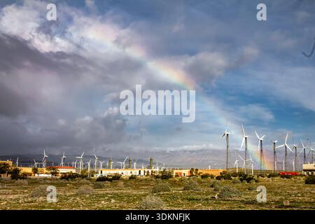 Joshua Tree National Park Rainbow is seen in the sky above a field of wind turbines. The scene is peaceful and serene, with the rainbow adding a touch Stock Photo