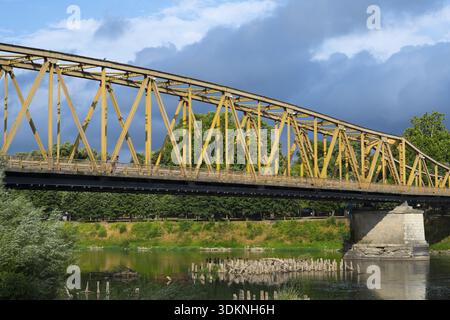 Yellow metal bridge over a river with green vegetation on the banks and cloudy sky, bridge over the Morava river, cuprija, Cuprija, Pomoravlje distri Stock Photo