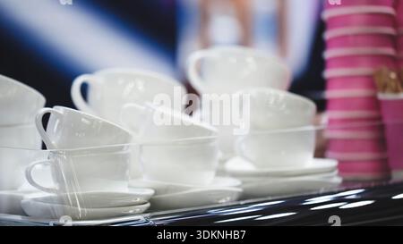 Row of white cups and saucers is lined up on coffee shop counter. cups are arranged neatly and orderly, some resting on saucers. concept is clean and Stock Photo