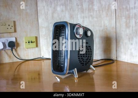 A blue, retro-style electric fan heater sits on a wooden surface with chrome details and two control knobs. Stock Photo