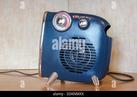 A blue, retro-style electric fan heater sits on a wooden surface with chrome details and two control knobs. Stock Photo