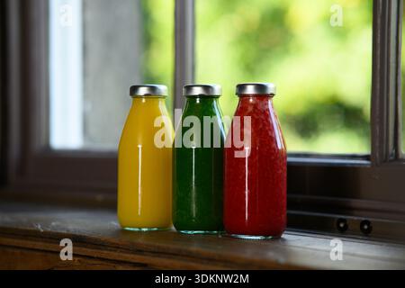 Three bottles of juice are lined up on a window sill. The bottles are different colors and are filled with different juices Stock Photo