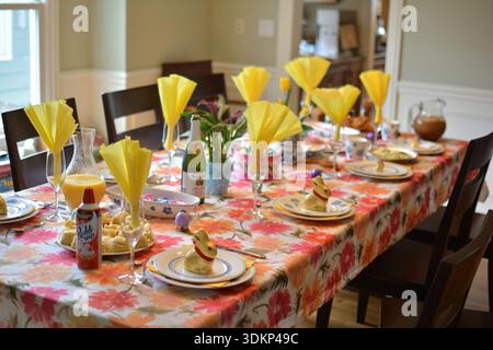 Fully set Easter dining table decorated with yellow napkins, dyed eggs, flowers, and festive spring decorations. Stock Photo