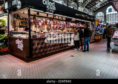 Shoppers browse the Oiled & Salt stall at the historic Mercat Central in Valencia, Spain, featuring gourmet olives, oils, and cured delicacies. Stock Photo