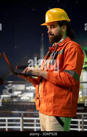 Industrial drilling barge crew member inspect equipment integrity using laptop software. Offshore platform worker performing machinery checkup with notebook program to ensure safety Stock Photo