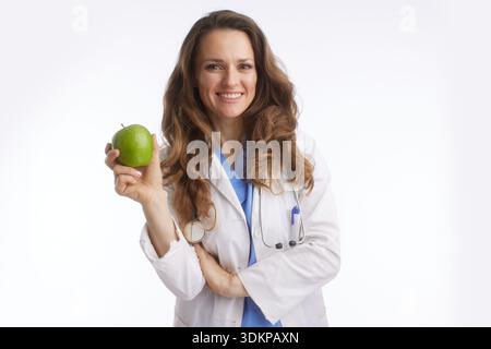 A professional female physician with a stethoscope holding a green apple, symbolizing nutrition, healthy lifestyle, and preventative medicine in a hea Stock Photo