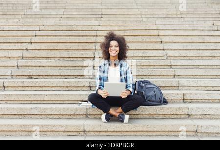 Smiling student sitting on stairs using laptop Stock Photo