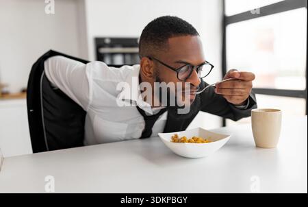 Black man rushing to work having breakfast at home Stock Photo