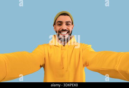 Happy middle eastern bearded man taking selfie, having fun, looking and smiling at camera, blue background Stock Photo