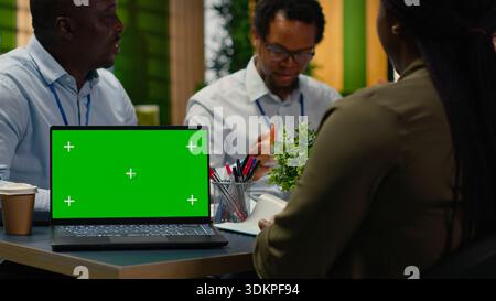 Green screen mockup laptop used by AI company admins discussing tech roadmap during briefing session. Workers developing apps using deep learning tech on chroma key notebook, camera B Stock Photo