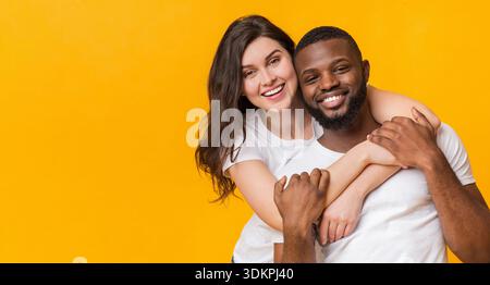 Portrait of happy multiracial couple embracing, posing together over yellow background Stock Photo