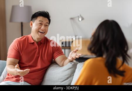 Positive asian man having conversation with woman, home interior Stock Photo