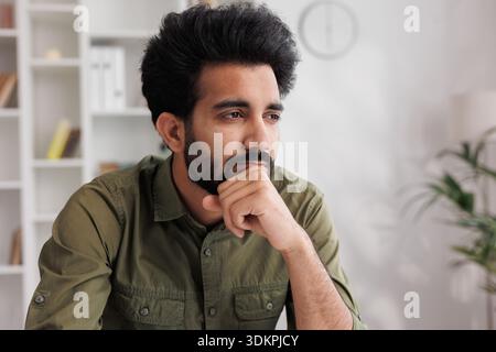 Bored millennial generation man sitting on sofa, feeling lonely at home. Unhappy young male suffering from negative thoughts, having depressive mood o Stock Photo