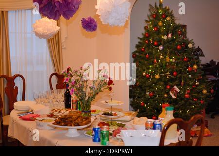 Festively set dining table with holiday food and decorated Christmas tree in a family home. Stock Photo