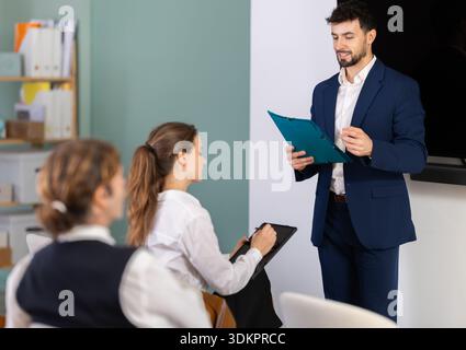 Male business trainer holding paper sheets explaining topic to professionals Stock Photo