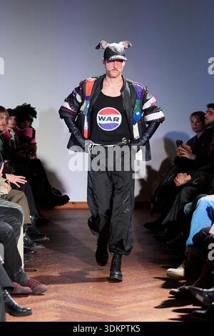 Berlin, Germany, 2nd Feb, 2026. A model walks the runway in a striking anti-war statement look at the PLNGNS AW26 show during Berlin Fashion Week. Part of the "ERROR AS ASSET" collection, the outfit features a black tank top with a prominent graphic circular print reading "WAR", layered under an oversized multi-colored patchwork jacket with quilted details. The styling includes black nylon cargo trousers, long black leather gloves, black boots, and a matching upcycled cap with animal ear features. Credit: Felix Wolf/Ģ����ý Live News Stock Photo
