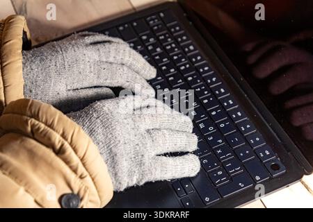 Side view close up of gloved hands working on a laptop during heating outage and power cuts in winter, capturing remote work and resilience Stock Photo