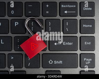 Red unlocked padlock with warning symbol on black computer keyboard background. Concept of cybersecurity threats, data breach, password leak, and onli Stock Photo