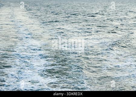 Aerial view of ocean waves with a foamy wake trailing through the water, showing dynamic sea movement and vessel impact. Stock Photo