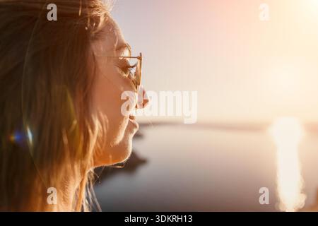 Woman sunset beach profile of a happy young woman wearing sunglasses enjoying the view of the ocean during golden hour Stock Photo