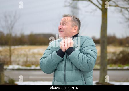 Thoughtful mature man standing outdoors in winter, holding his jacket collar and looking upward with a calm, reflective expression in a natural rural Stock Photo