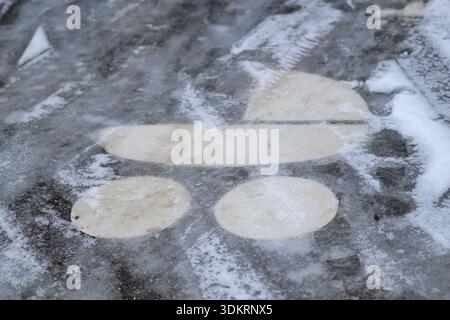 Frozen close-up of a wheelchair parking symbol partially covered by ice and snow on winter pavement. Stock Photo