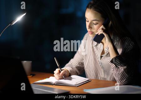 Self employed scheduling in agenda talking on phone working in the night Stock Photo